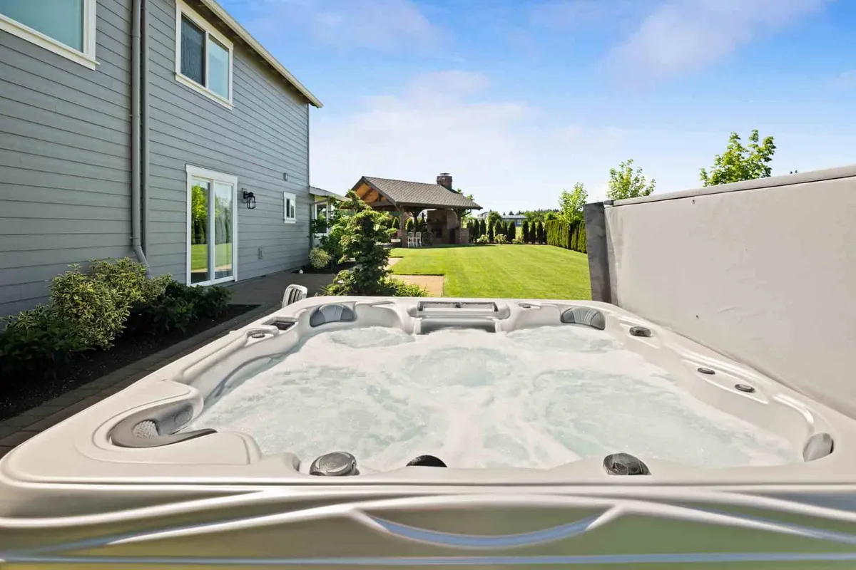 A serene hot tub nestled beside a manicured lawn and outdoor structure, with wide views over the surrounding orchard landscape. The setting is tranquil, perfect for soaking while taking in sunset views or enjoying morning coffee outdoors.