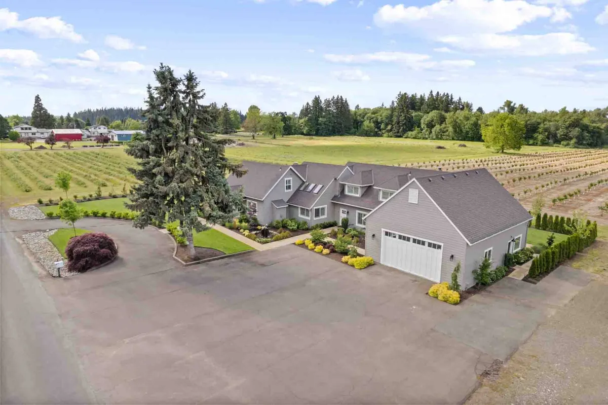 This wide-angle exterior view captures the large estate home set among landscaped gardens, tall trees, and an adjoining vineyard. The tranquil, secluded acreage provides privacy while inviting guests to take in orchard and vineyard views.