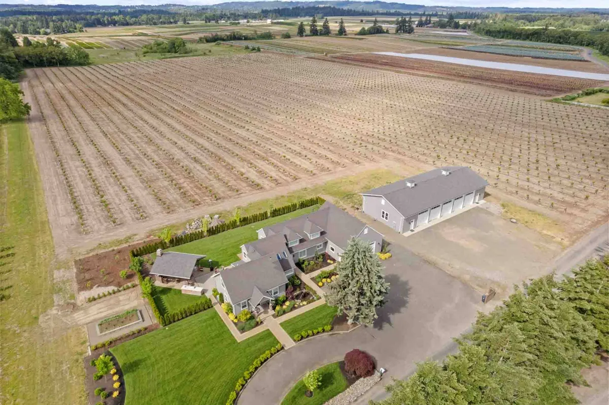 The image captures the main house surrounded by vineyard fields, landscaped gardens, and an outbuilding, all under an open sky. The spacious grounds and lush landscaping highlight the property's openness, providing an inviting environment for outdoor adventures with pets and family gatherings.