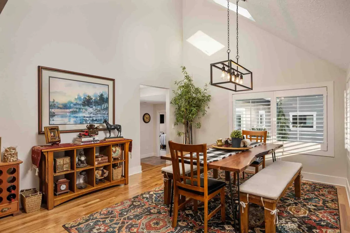 A warmly lit dining area featuring a large dining table ready for communal meals, with inviting artwork on the walls and a large window letting in natural light. The setup encourages shared dining and celebration in a welcoming atmosphere.