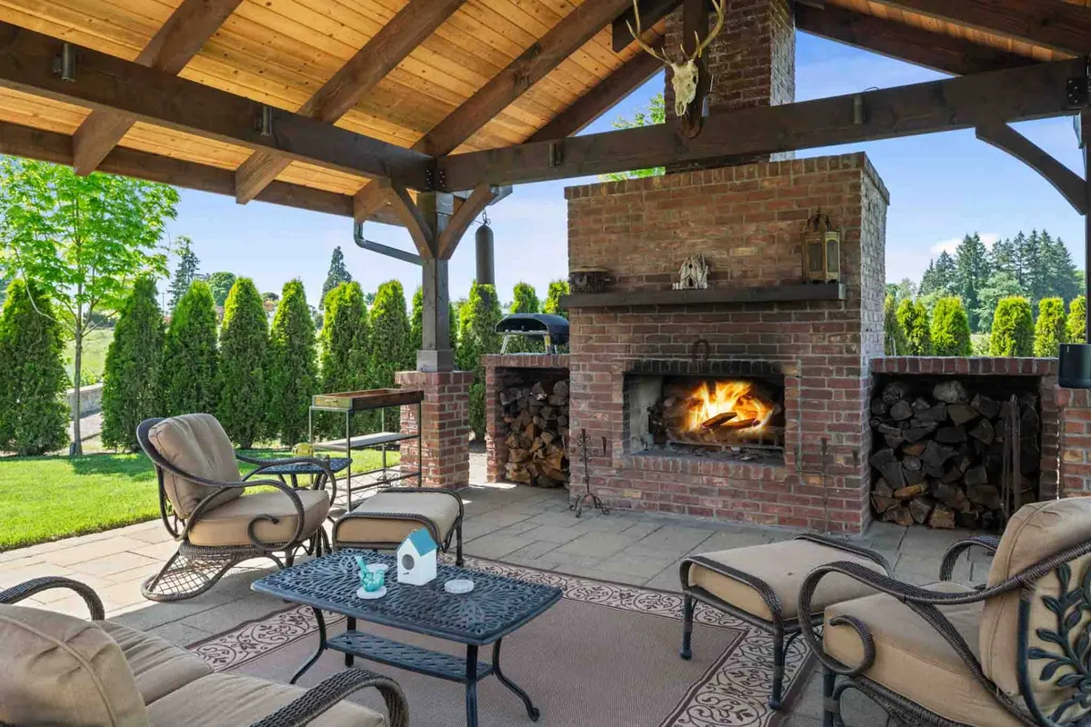 This exterior image centers on a cozy fireplace surrounded by comfortable seating and a wood stack, complemented by decorative elements that create a welcoming outdoor gathering spot. The setting exudes relaxation and is ideal for both intimate and larger social gatherings.