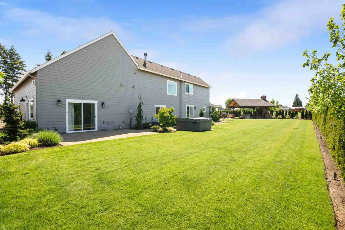 A manicured lawn and inviting patio area are framed by an outdoor structure, likely a pergola or gazebo. The space is ideal for gatherings, and the open surroundings offer both privacy and connection to the orchard beyond.