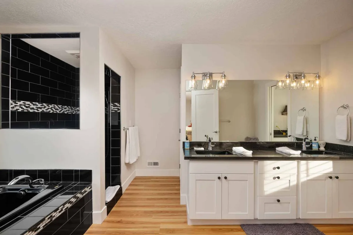 A spacious, elegant bathroom featuring a double sink vanity, a black tiled shower, and a freestanding bathtub. The calming color palette and refined fixtures suggest both privacy and indulgence, hinting at the luxury of private bathrooms in every bedroom.